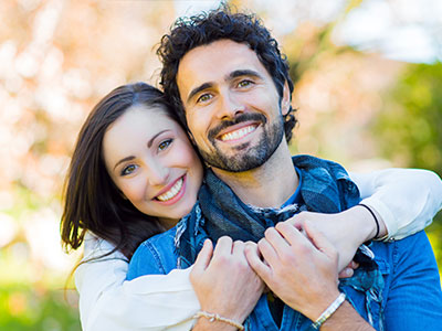 The image shows a man and a woman posing for the camera with smiles, both wearing casual attire.