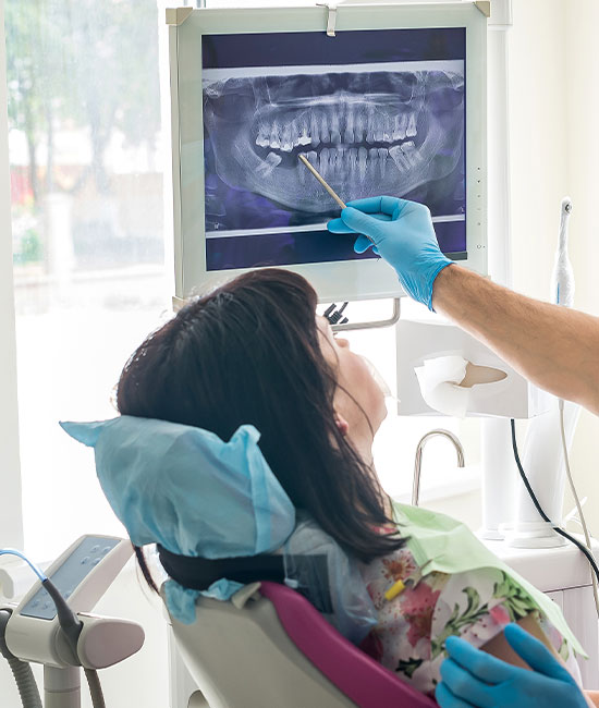 The image depicts a dental setting where a person is seated in a dental chair, receiving oral care. A dental hygienist is seen using a dental mirror to inspect the patient s teeth and gums.