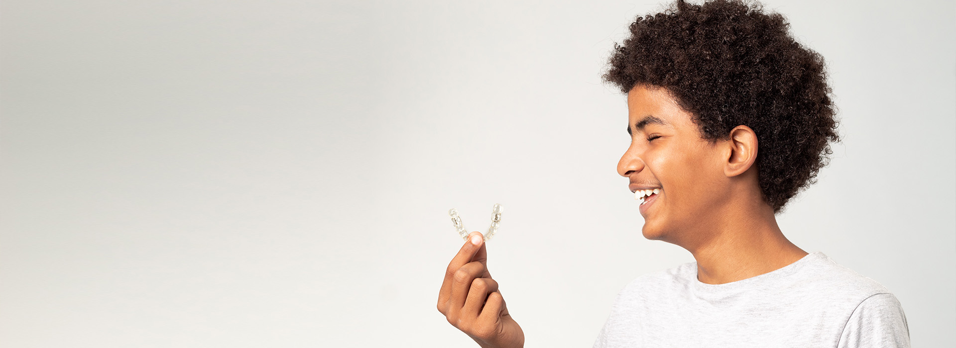 The image features a young person holding a small white object, likely a flower or petal, with a joyful expression. They are standing against a plain background, which highlights their presence and the object in their hand.