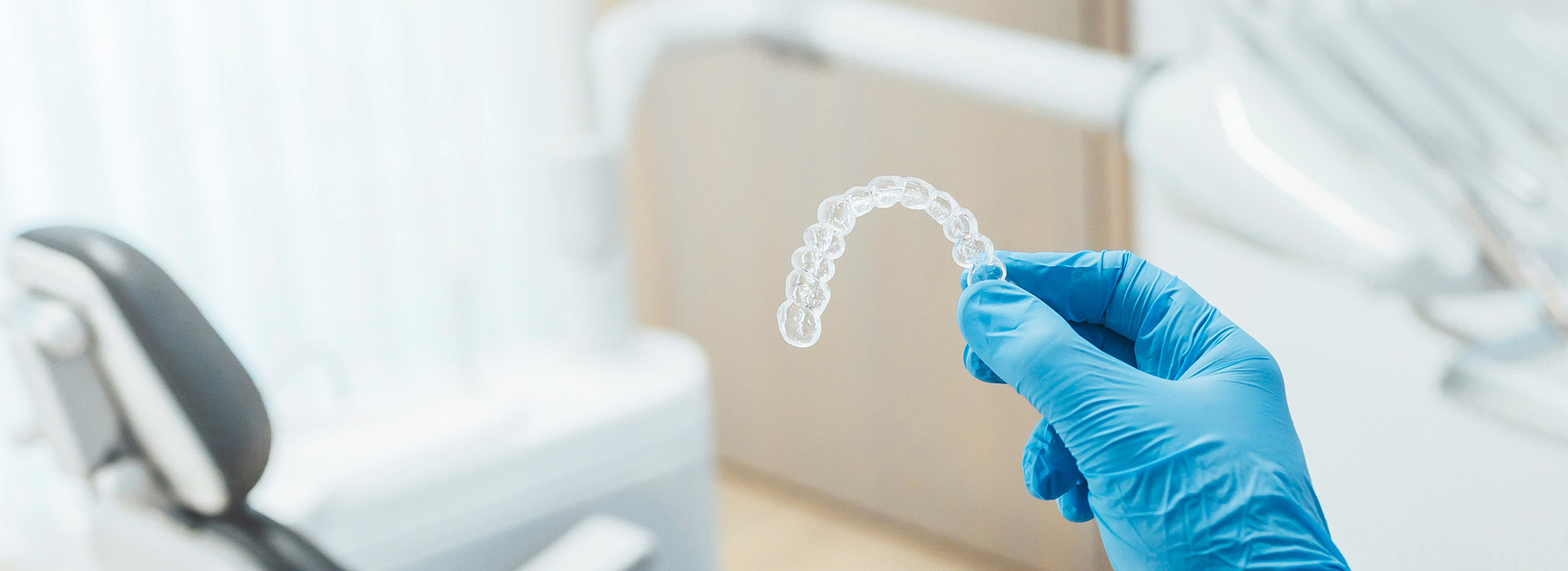 A medical professional in a white lab coat holding a transparent object, likely a dental implant or bridge, against a blurred background of a dental office setting.