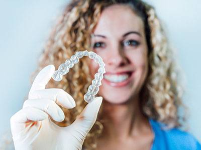 Woman holding a transparent dental retainer with a smile.