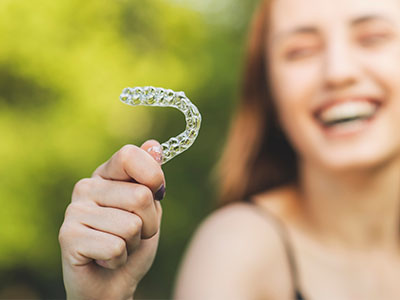 An image of a smiling woman holding a clear retainer with the word alt written on it.