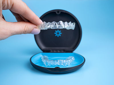 The image shows a human hand holding an open blue and black dental impression tray, with the tray s interior containing a transparent dental impression material.